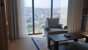 A modern living room with a large window, a sofa, a coffee table, and a patterned rug.