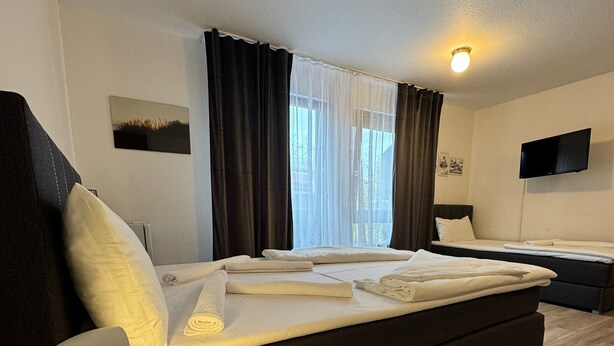 Una habitación de hotel moderna con una cama grande, una cama más pequeña, un televisor de pantalla plana y una mesita de noche con lámpara.