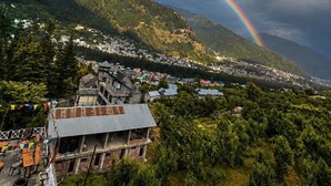 Paesaggio montuoso con un arcobaleno, case e un edificio con tetto spiovente.