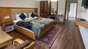 Una camera da letto con un letto, comodino, sedia, pavimento in legno, ventilatore a soffitto e televisore montato a parete.