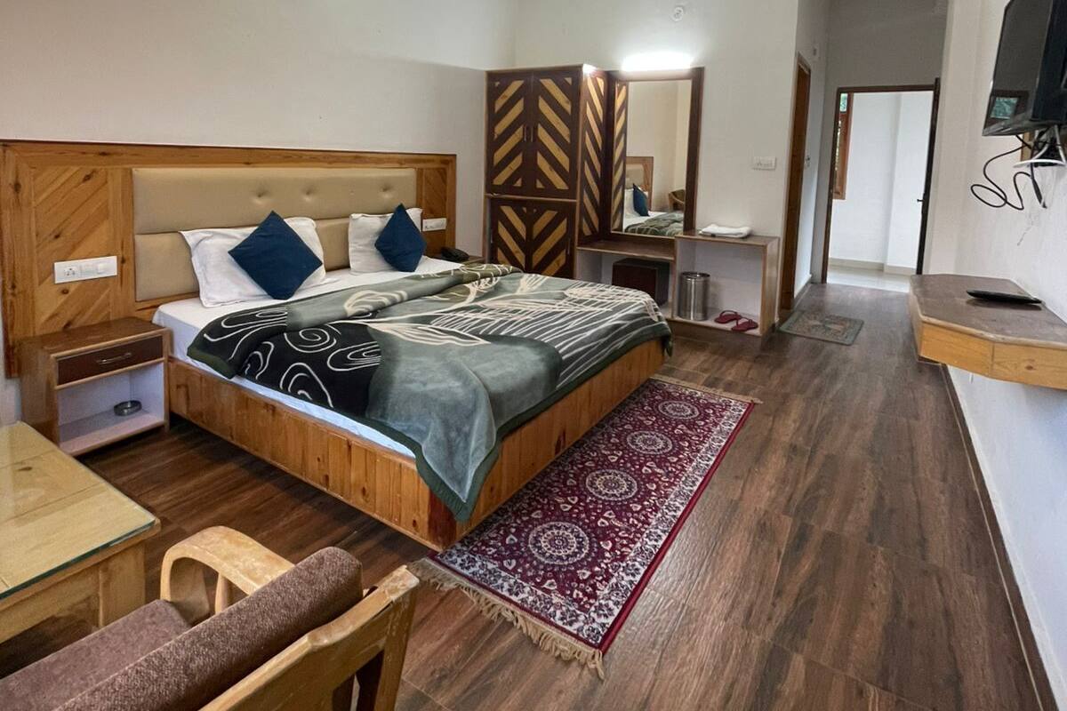 A bedroom with a bed, bedside table, chair, wooden floor, ceiling fan, and a TV mounted on the wall.