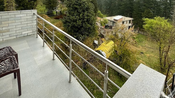 Un balcone con ringhiera metallica, una sedia e vista su un paesaggio montuoso con alberi e un edificio.