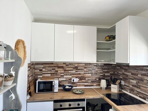 A modern kitchen with white cabinets, a microwave, a stove, and a stone backsplash. - Newly renovated single-story house, a 6-minute walk to Los Locos Beach. (Torrevieja)