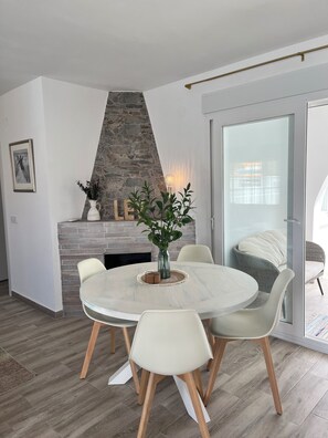 A dining area with a round table, chairs, a vase with plants, a stone fireplace, and a framed picture on the wall. - Newly renovated single-story house, a 6-minute walk to Los Locos Beach. (Torrevieja)