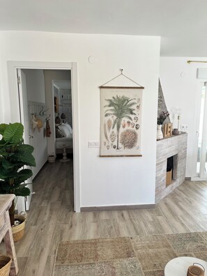A modern living room with a fireplace, a large framed botanical print, and a view into the adjacent bedroom. - Newly renovated single-story house, a 6-minute walk to Los Locos Beach. (Torrevieja)