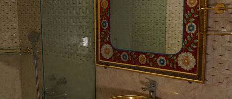 A bathroom with a glass shower enclosure, a gold sink, and a decorative mirror with floral patterns.