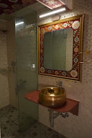 Un baño con cabina de ducha de vidrio, lavamanos dorado y espejo decorativo con motivos florales.