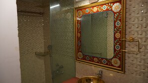 Et badeværelse med glasbrusekabine, toilet og håndvask med et dekorativt spejl.