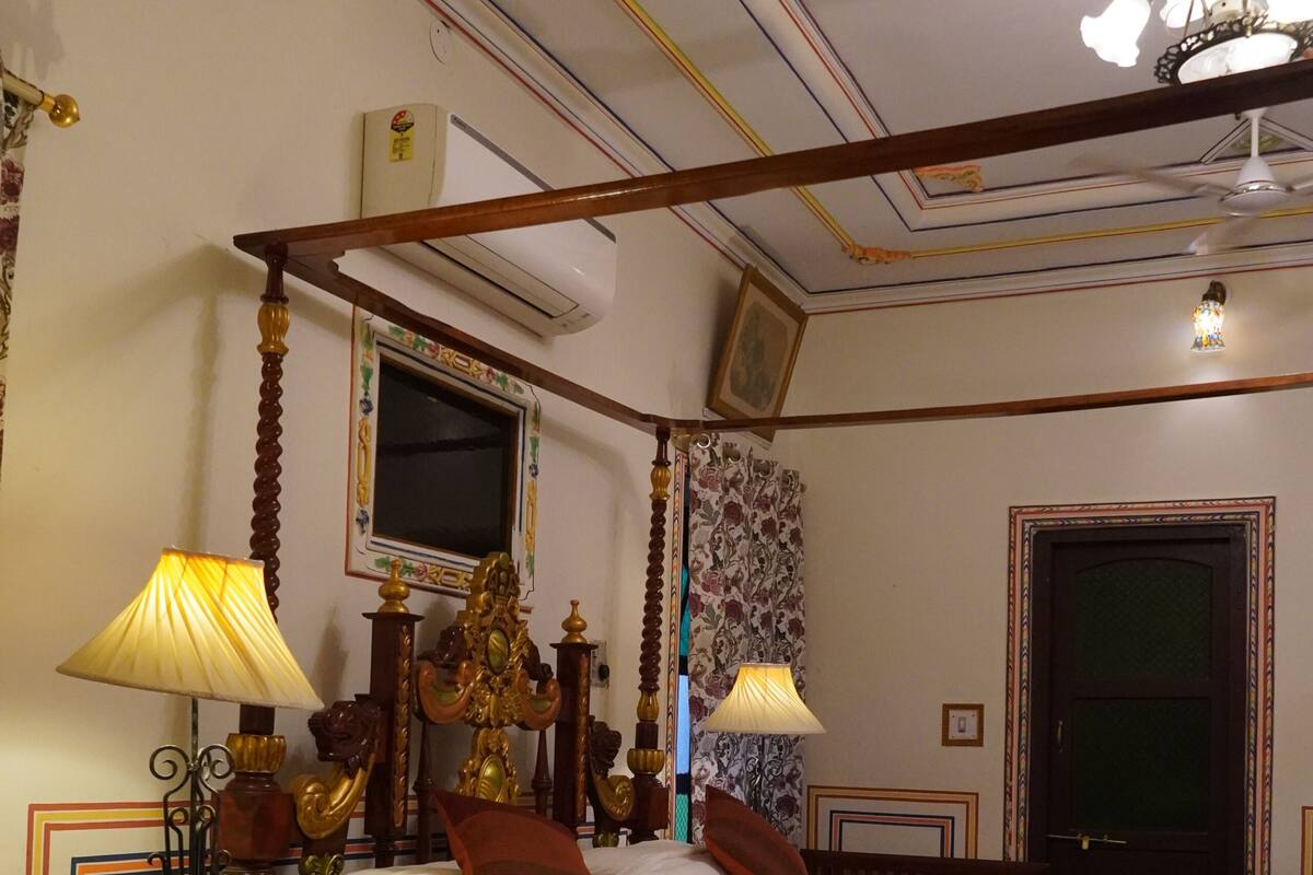 Ein Bett mit Baldachin, darüber ein Fernseher, eine Kristallleuchter und eine Holzbalkendecke mit dekorativen Stuckverzierungen.