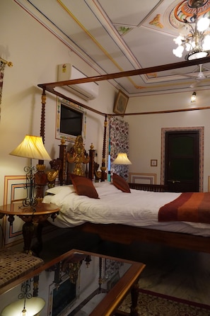 Una cama con dosel, un televisor en la parte superior, una araña y un techo de madera con molduras decorativas.