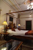 Una cama con dosel, un televisor en la parte superior, una araña y un techo de madera con molduras decorativas.