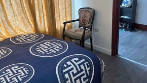 Ein Hotelzimmer mit Bett, Sessel, Fernseher und einer Tür zu einem Flur.