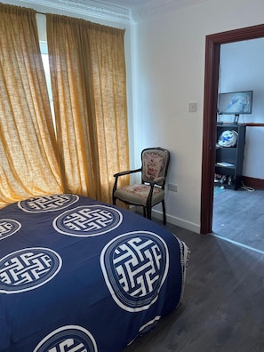 Una habitación de hotel con cama, sillón, televisor y puerta que da a un pasillo.