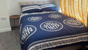 Ein Bett mit geometrischem Muster auf der Bettdecke, ein Sessel und ein Vorhang.