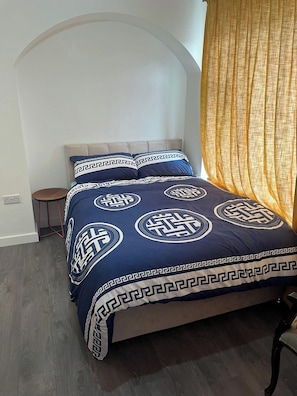 Una cama con una colcha de estampado geométrico, una silla y una cortina.