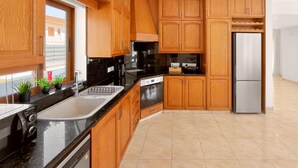 A modern kitchen with wooden cabinets, a stainless steel refrigerator, and a window with potted plants. - Delina Coastal Villa Steps from Everything (Protaras)