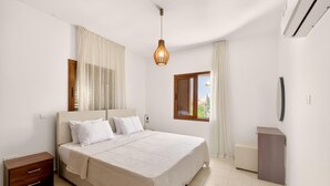 A bedroom with a bed, a nightstand, a bedside table, a window with curtains, and a wall-mounted air conditioning unit. - Delina Coastal Villa Steps from Everything (Protaras)