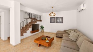 A modern living room with a staircase, a flat-screen TV, a wooden coffee table, and a beige sofa. - Delina Coastal Villa Steps from Everything (Protaras)