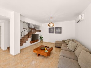 A modern living room with a staircase, a flat-screen TV, a wooden coffee table, and a beige sofa. - Delina Coastal Villa Steps from Everything (Protaras)
