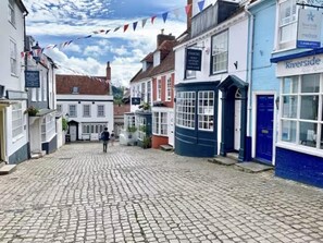 A cobblestone street lined with traditional buildings, a clock tower, and a sign for Riverside Medispa. - Lymington 1-bed Apt, Sleeps 3 With Parking (Lymington)