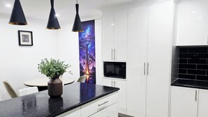 A modern kitchen with white cabinets, a black countertop, and a microwave. There is a framed quote on the wall and a potted plant on the counter.