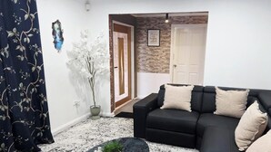 A living room with a black sofa, decorative pillows, a potted plant, and a patterned rug.