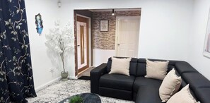 Een woonkamer met een zwarte bank, decoratieve kussens, een potplant en een kamerbreed tapijt.