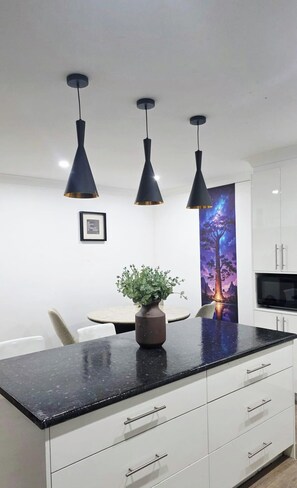 Een moderne keuken met een zwart aanrecht, witte kastjes en drie hanglampen.