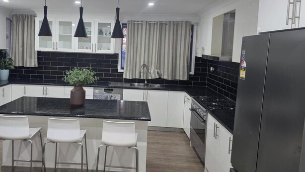A modern kitchen with a central island, white cabinets, black countertops, and a stainless steel refrigerator.