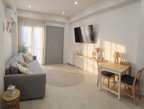 Ein modernes Wohnzimmer mit einer Couch, einem Esstisch, Stühlen, einem Fernseher und einem kleinen Beistelltisch.