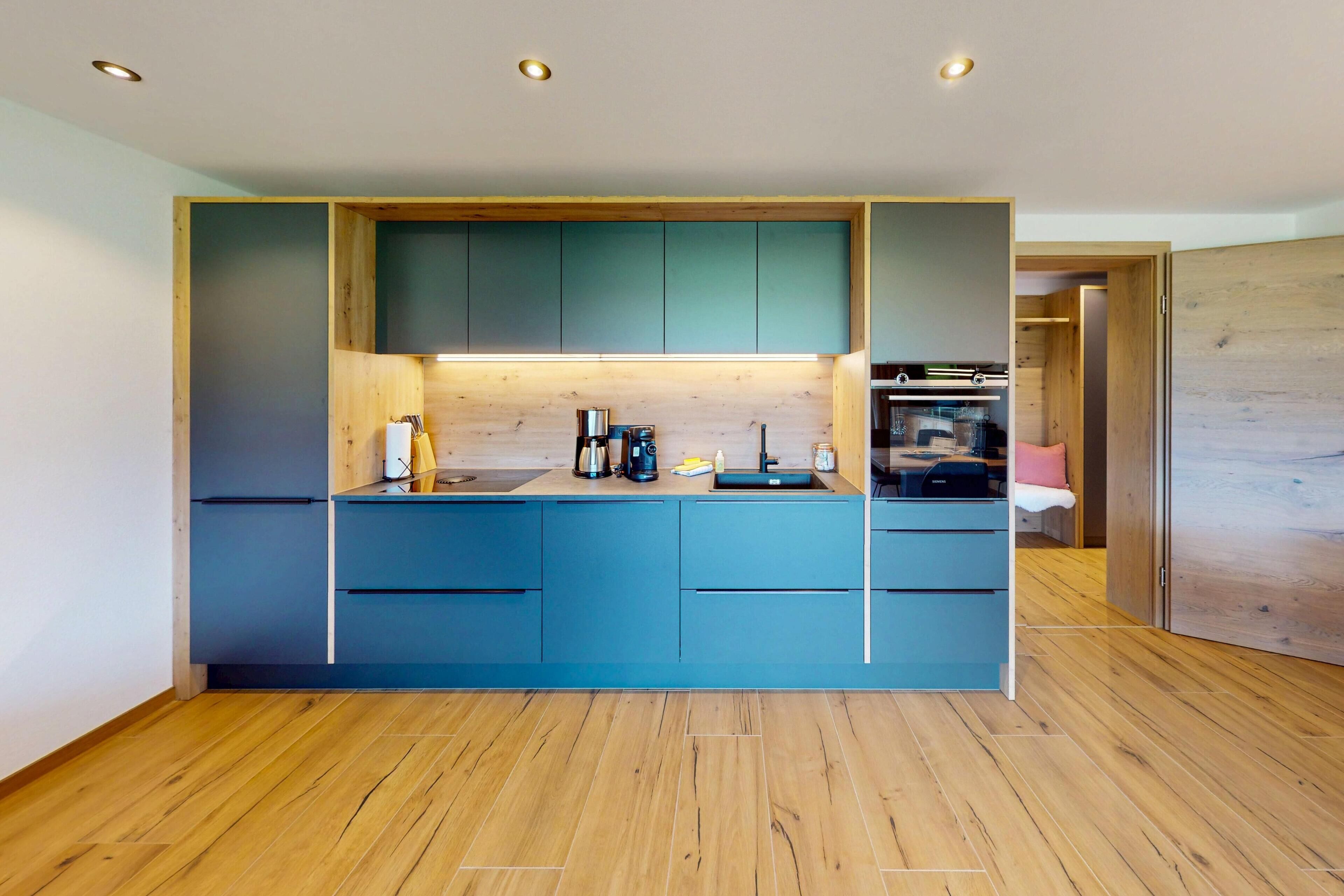 Eine moderne Küche mit blauen Schränken, Holzböden und eingebauten Geräten.