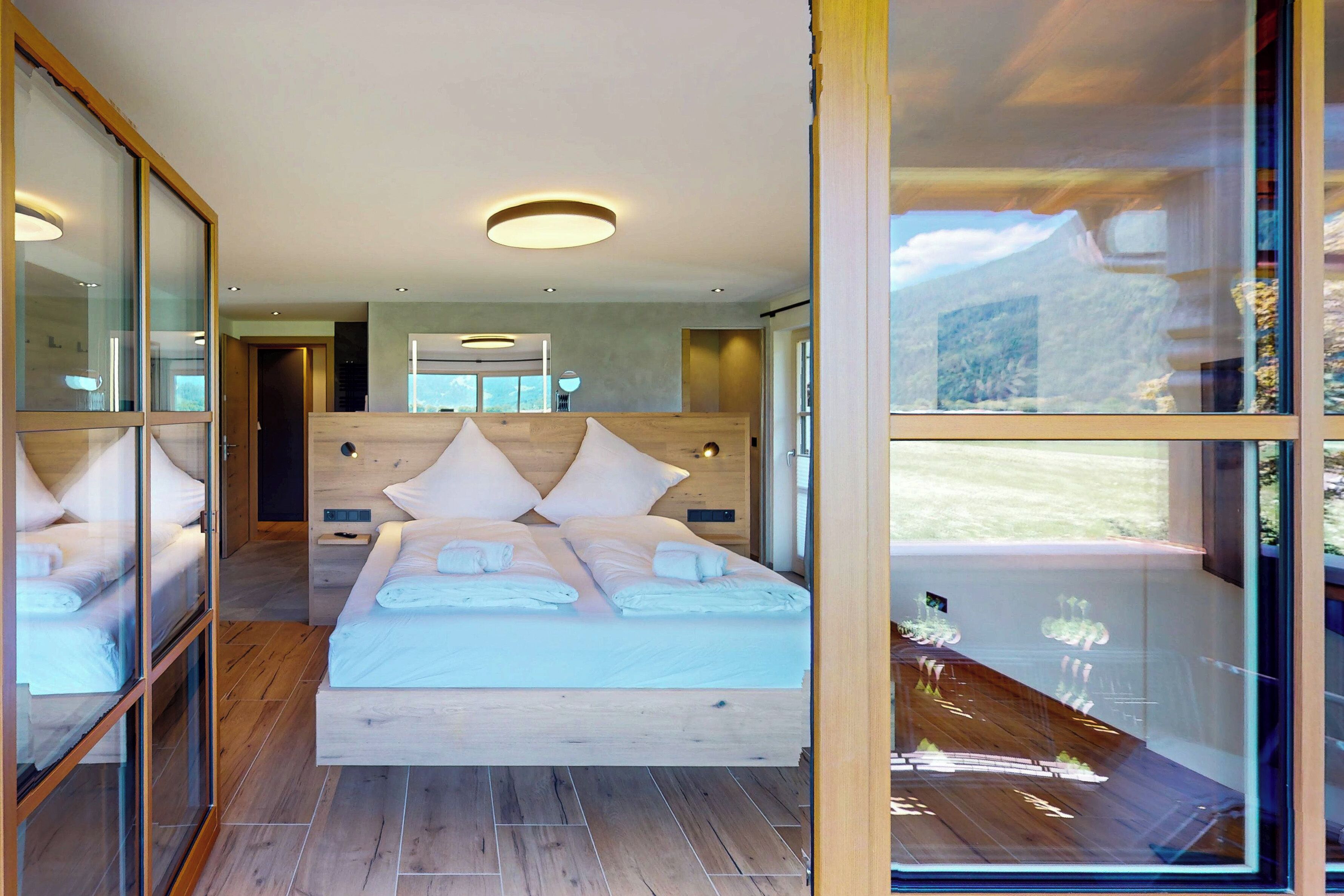 Ein modernes Schlafzimmer mit einem großen Bett, einem Holz-Kopfteil und einer Glastür, die auf einen Balkon mit Bergblick führt.
