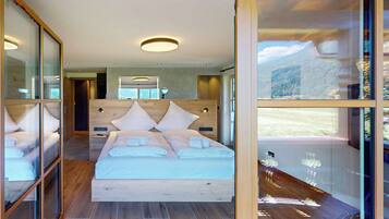 Ein modernes Schlafzimmer mit einem großen Bett, einem Holz-Kopfteil und einer Glastür, die auf einen Balkon mit Bergblick führt.