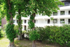 Ein mehrgeschossiges Gebäude mit weißer Fassade, umgeben von Bäumen und einem Holzzaun.