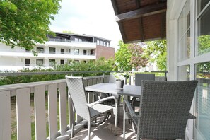 Ein Balkon mit Korbmöbeln, einer Topfpflanze und Blick auf ein mehrgeschossiges Gebäude.