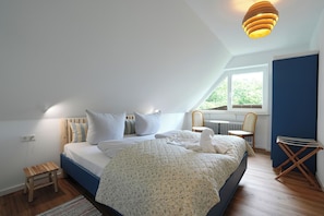 Ein Schlafzimmer mit Bett, Hocker, Stuhl, Fenster und Heizkörper.