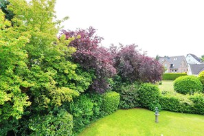 Ein gepflegter Garten mit verschiedenen Bäumen und Sträuchern, einer Rasenfläche und einer Statue.