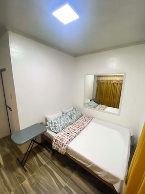 Una cama individual con almohadillas estampadas, una mesita de noche, un espejo y una ventana con cortinas.