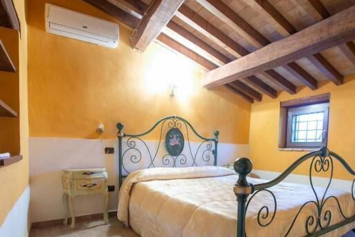 A bedroom with a bed, a nightstand, a window, and a wooden ceiling.