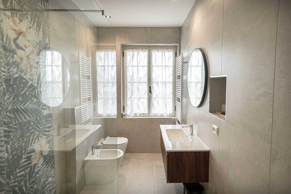 A modern bathroom with a bathtub, two sinks, a toilet, and a large mirror.