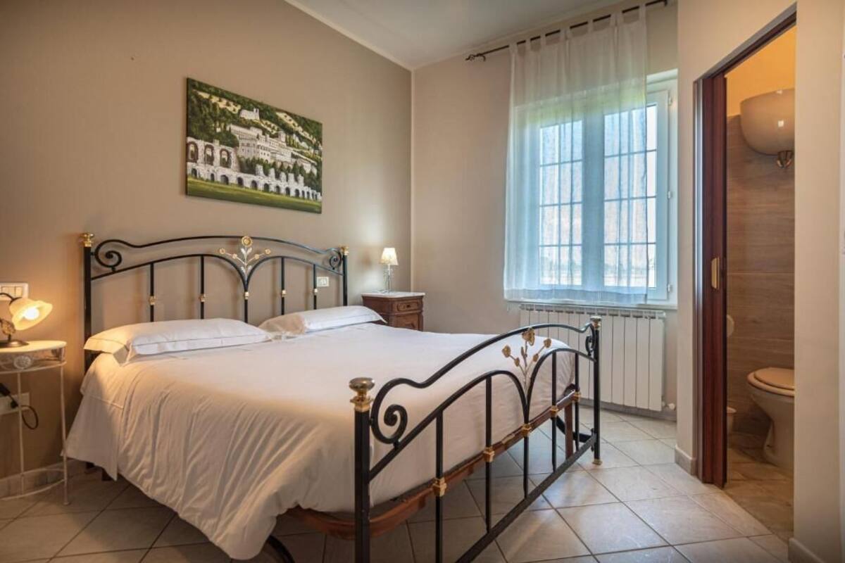 A bedroom with a bed, a nightstand, a lamp, a window with curtains, and a radiator.