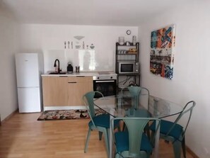 Eine kleine Küche mit Kühlschrank, Mikrowelle und Herd. Ein Esstisch mit Stühlen und ein Teppich sind ebenfalls vorhanden.
