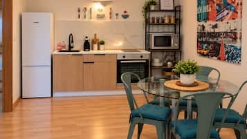 Una cocina moderna con refrigerador, estufa, microondas y una mesa de vidrio con sillas.