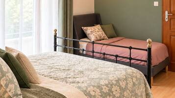 A bedroom with a double bed, a bedside table, a nightstand, a window with curtains, and a wall-mounted light.