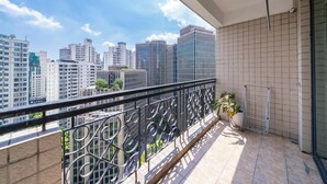 Un balcón con barandilla metálica, una planta en maceta y vistas de edificios altos.