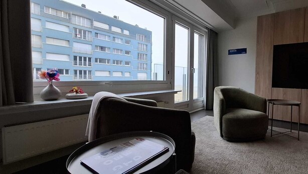 Ein Hotelzimmer mit großem Fenster, Flachbildfernseher, Sofa und kleinem Tisch.