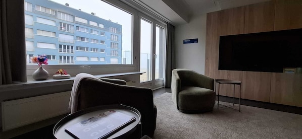 Ein Hotelzimmer mit großem Fenster, Flachbildfernseher, Sofa und kleinem Tisch.