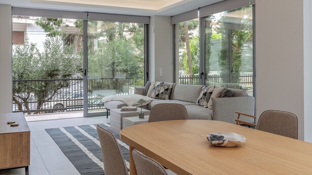 A modern living room with a sofa, a dining table, and a view of the outdoors through large windows.