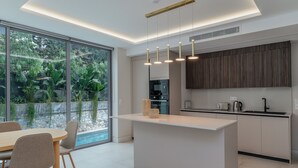 A modern kitchen with a central island, large windows, and a dining area with chairs.
