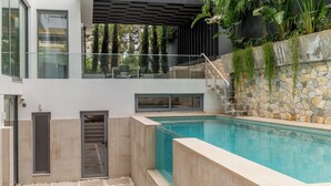 A modern outdoor pool area with a stone wall, a glass balustrade, and a pergola.